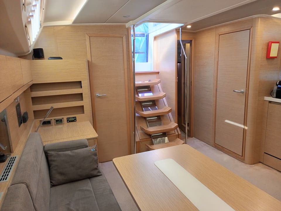 2022 Hanse 508 – açık meşe salon, gri kanepe, masa, kokpite çıkan merdiven ve kabin kapıları