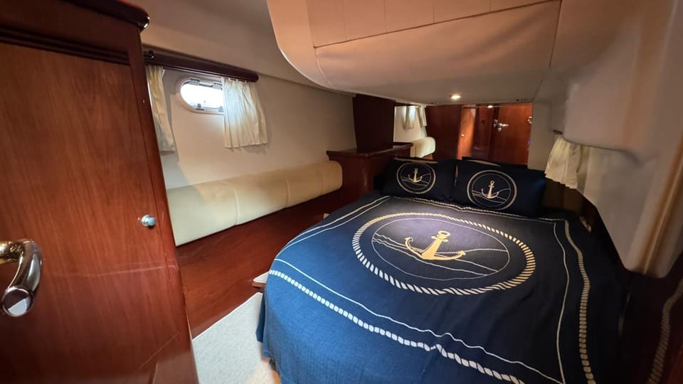 2002 Prestige 46 – cabin with double bed, anchor-themed navy bedding, side settee, portholes and warm wood joinery