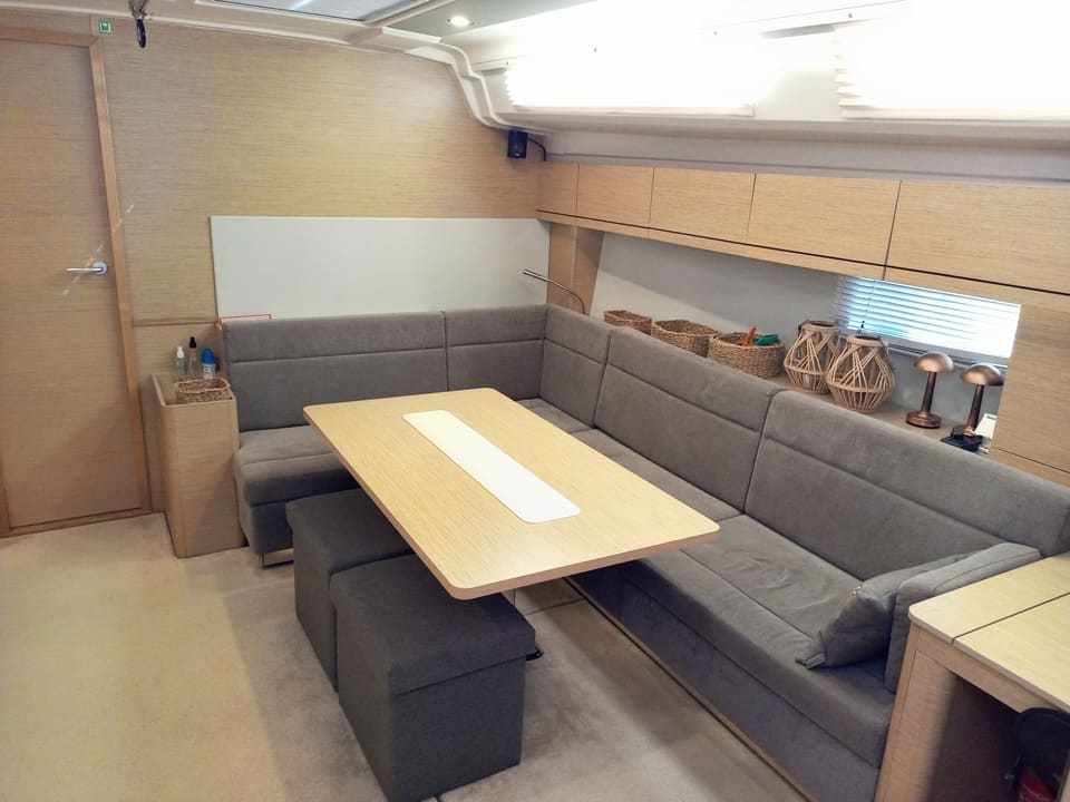 2022 Hanse 508 – U şeklinde gri koltuk, açık renk ahşap masa ve pufların bulunduğu salon