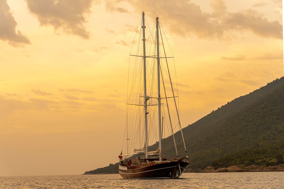 2009 Custom Ketch 31M – two-masted ketch at anchor on calm water at golden sunset beside a green hillside