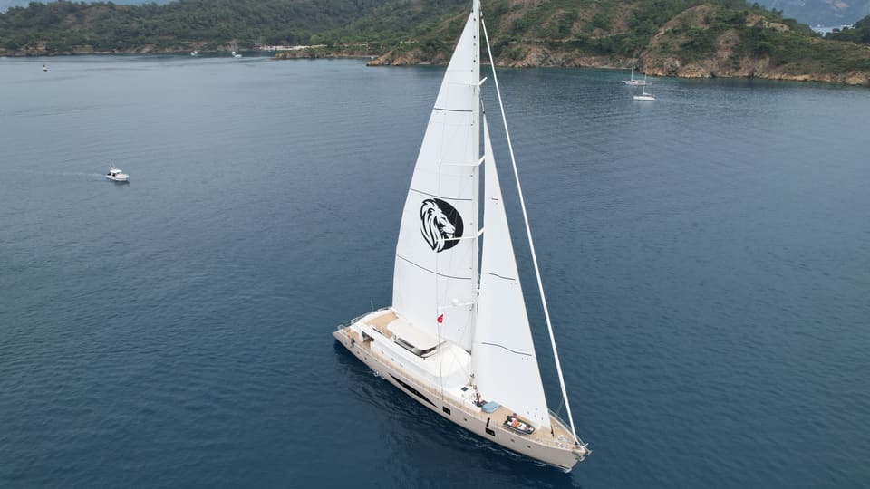 2023 Custom Laminated Motorsailer 41M – aerial view under full sail with white mainsail and jib on calm blue water