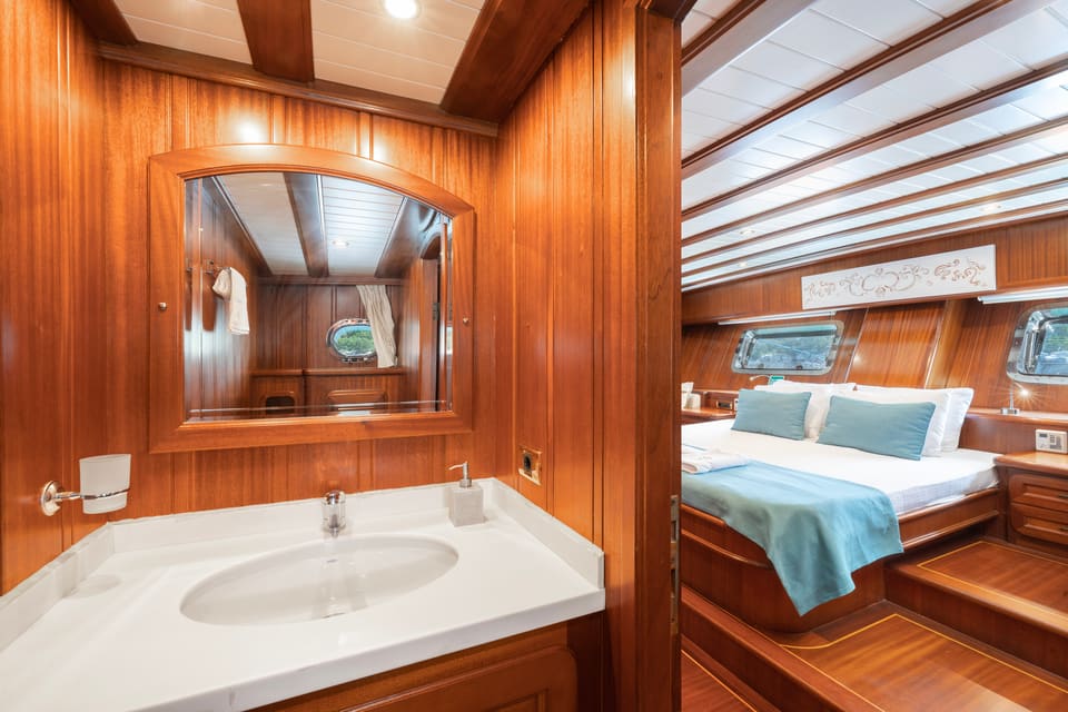 2009 Custom Ketch 31M – en-suite bathroom with washbasin and mirror opening to a cabin with double bed and warm wood panelling