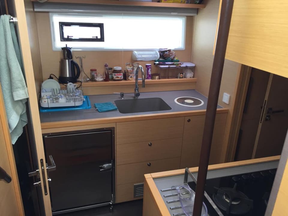 2015 Lagoon 560 S2 – eviye, indüksiyon ocak, buzdolabı, ahşap dolaplar ve pencereli kompakt mutfak
