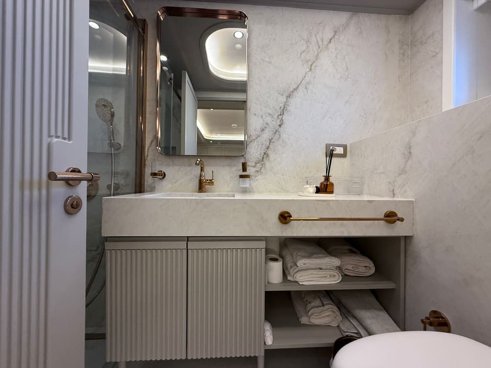 2023 Custom Laminated Motorsailer 41M – bathroom with marble walls, fluted vanity, gold fixtures and glass shower