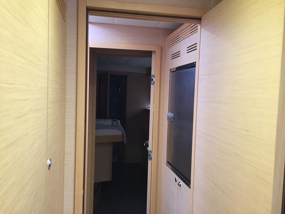 2015 Lagoon 560 S2 – açık ahşap kaplamalı gövde koridoru, dolaplar ve kabine açılan kapı