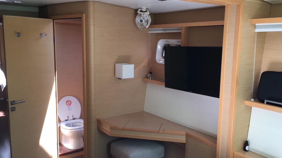 2012 Lagoon 560 – ahşap detaylı kabin, köşe çalışma masası, duvara monte TV ve kabine bağlı tuvalet