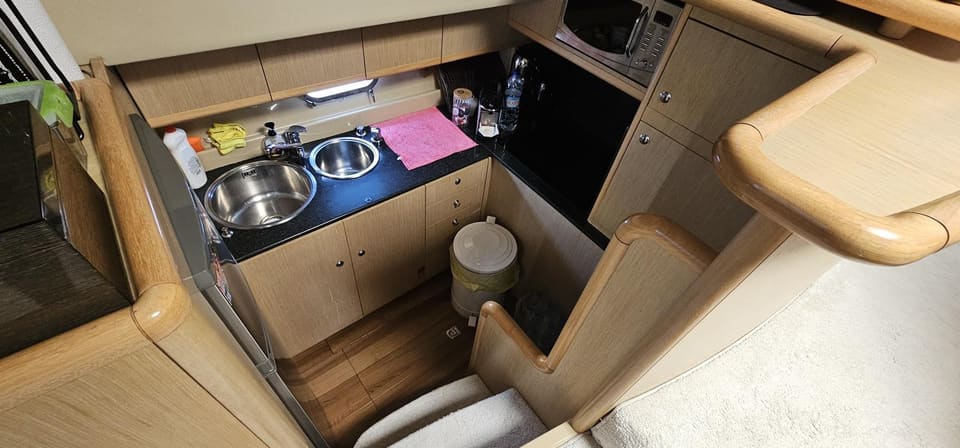 2005 Ferretti 530 – galley with double stainless sink, black countertop, cream cabinetry, microwave and wooden floor