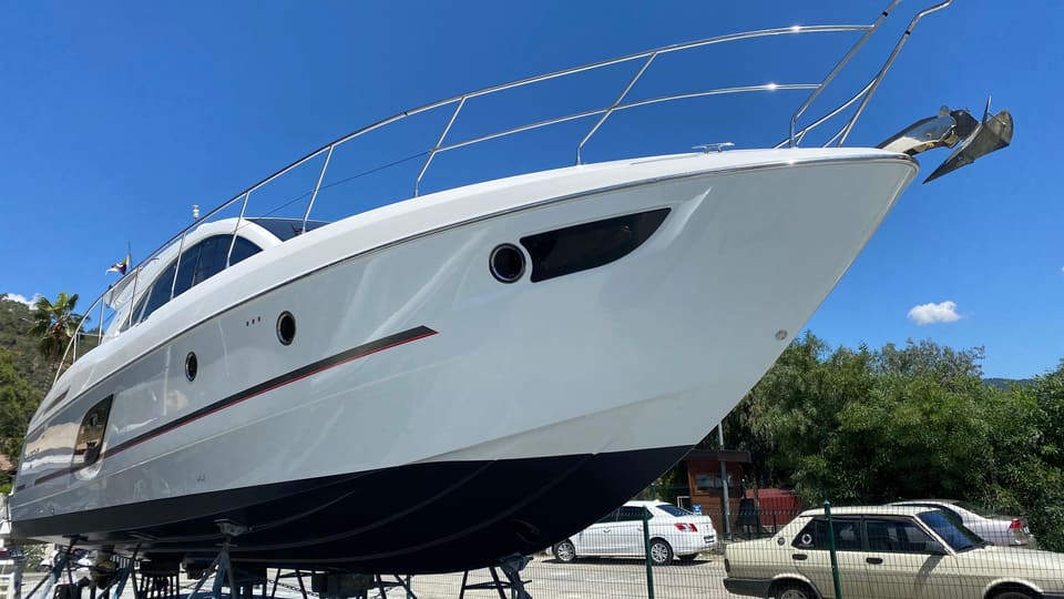 2014 Beneteau Gran Turismo 49 – karada sehpalar üzerinde beyaz tekne gövdesi ve baş, koyu zehirli boya ve paslanmaz baş küpeştesi