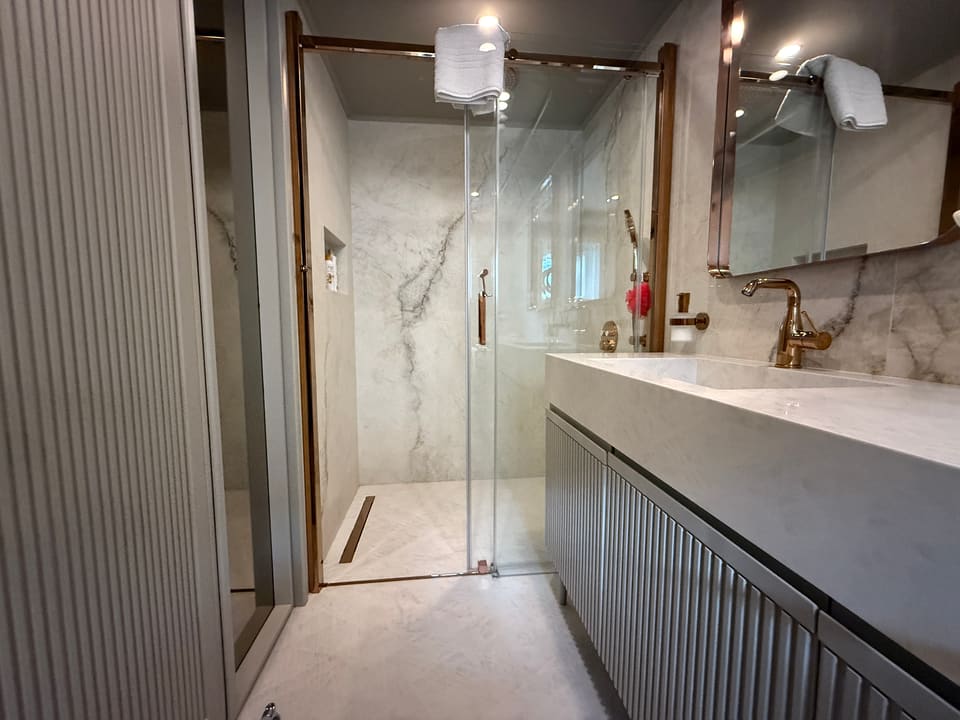 2023 Custom Laminated Motorsailer 41M – bathroom with marble walk-in shower, glass doors, gold fixtures and fluted vanity