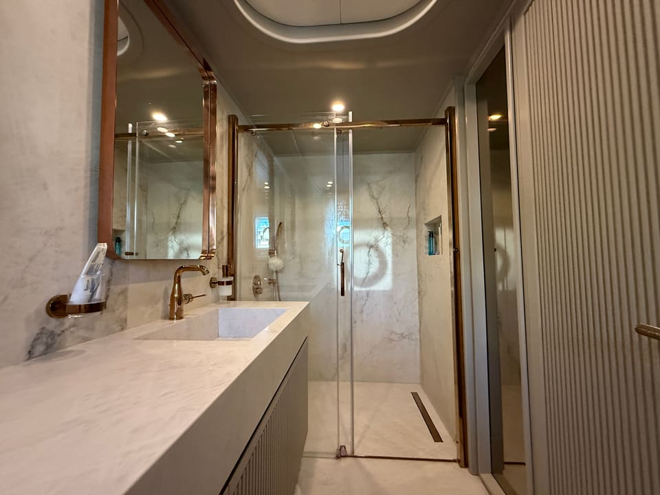 2023 Custom Laminated Motorsailer 41M – bathroom with marble walls, rose gold fittings, long vanity and glass walk-in shower