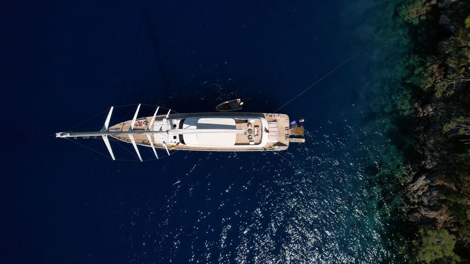 2023 Custom Laminated Motorsailer 41M – aerial top-down view of the sailing yacht at anchor in deep blue water beside a wooded shore