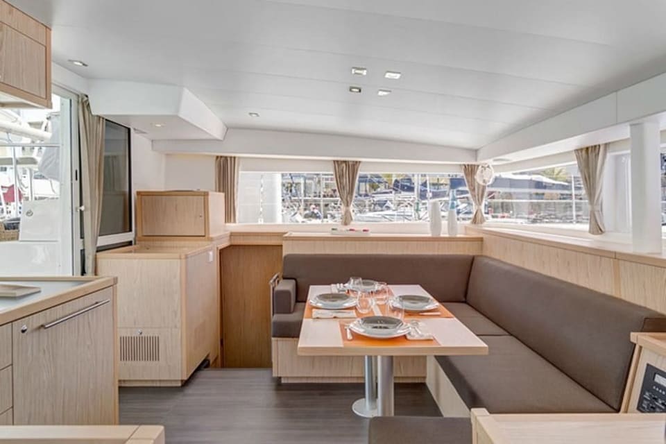 2010 Lagoon 400 – saloon with U-shaped grey sofa, dining table set for four, light wood joinery and panoramic windows