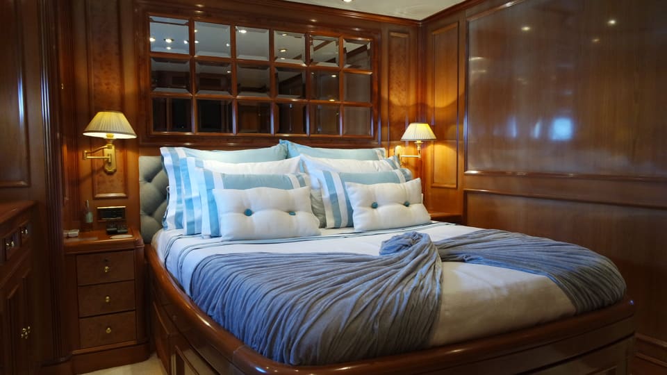 2003 Benetti Classic 115 – guest cabin with double bed, glossy wood panelling, blue throws and brass reading lamps