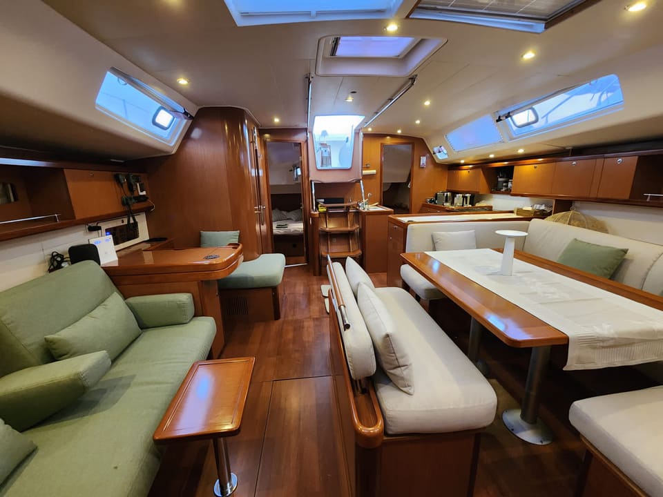 2009 Beneteau Oceanis 54 – yeşil koltuklu salon, yemek masası, tik ahşap detaylar ve tavan lombozları, arkada mutfak ve baş kabin