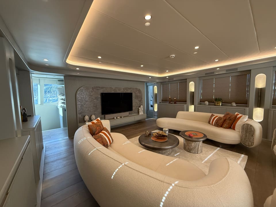 2023 Custom Laminated Motorsailer 41M – saloon with curved cream sofas, orange cushions, round coffee tables and wall-mounted TV