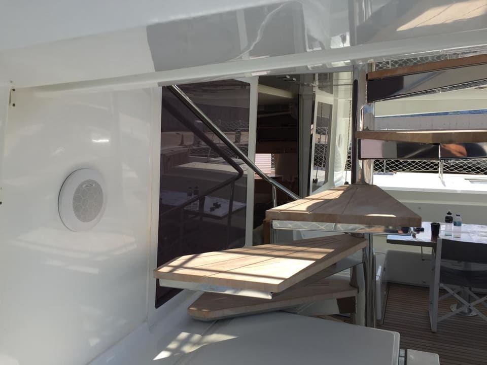 2015 Lagoon 560 S2 – flybridge'e çıkan tik basamaklı merdiven ve dış yemek masasıyla kıç kokpit