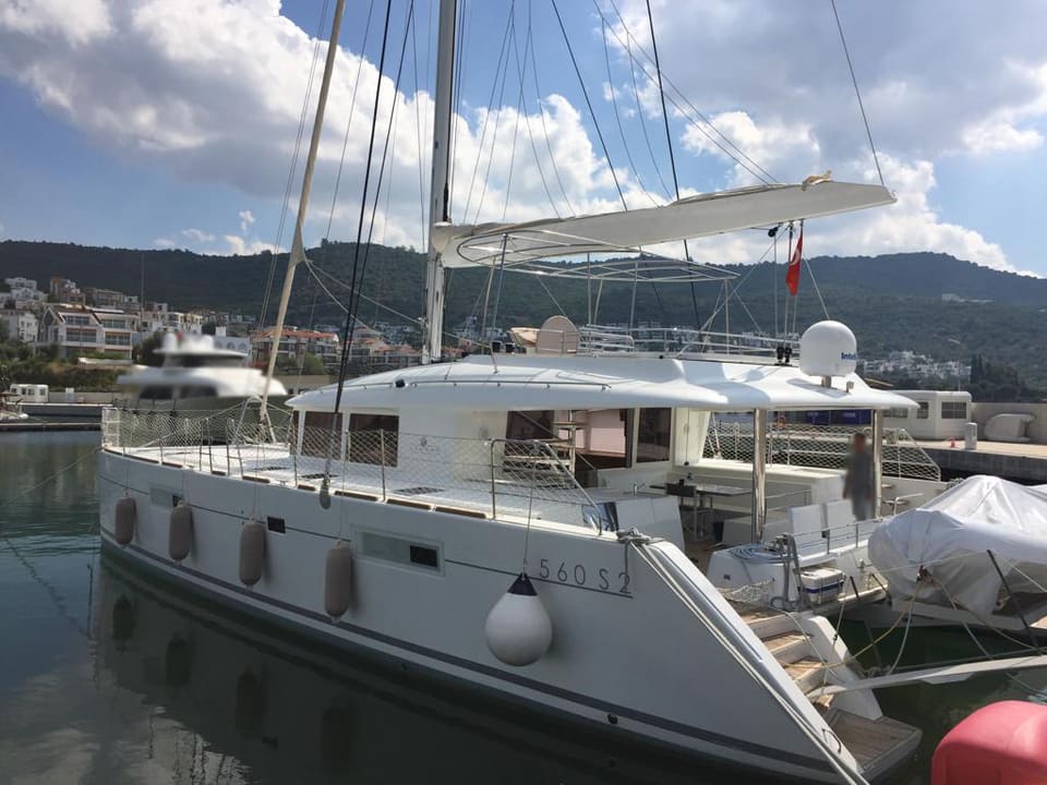 2015 Lagoon 560 S2 – kıçtan bağlı beyaz yelkenli katamaran; gövde, üst yapı, flybridge tenteleri ve yüzme merdiveni