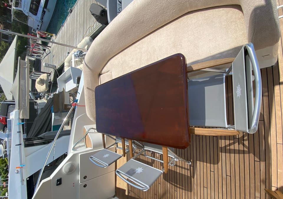 2014 Beneteau Gran Turismo 49 – ahşap yemek masası, minderli oturma grubu, katlanır sandalyeler ve tik güverteli kıç güverte