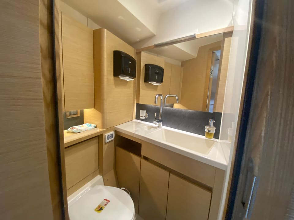 2018 Hanse 548 – bathroom with light wood cabinetry, vanity sink, mirror and marine toilet