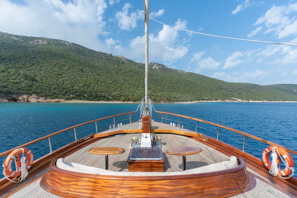 2009 Custom Ketch 31M – foredeck with curved varnished seating, teak tables, bowsprit and life rings overlooking the sea