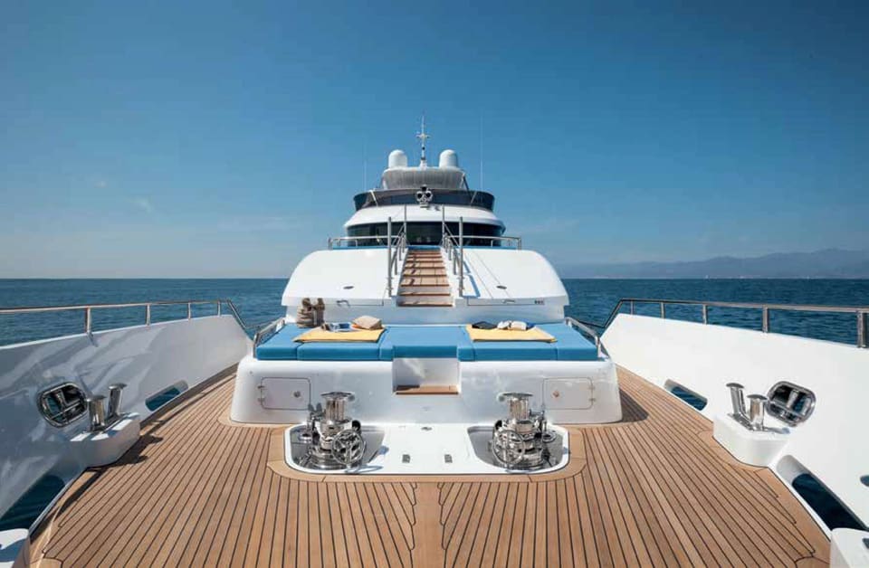 2016 Benetti Tradition Supreme 108 – tik kaplı baş güverte, mavi güneşlenme minderleri, ırgatlar ve üst güverteye çıkan merdiven