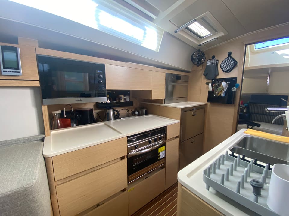 2018 Hanse 548 – galley with light wood cabinetry, microwave, oven, stovetop, double sink and overhead hatches