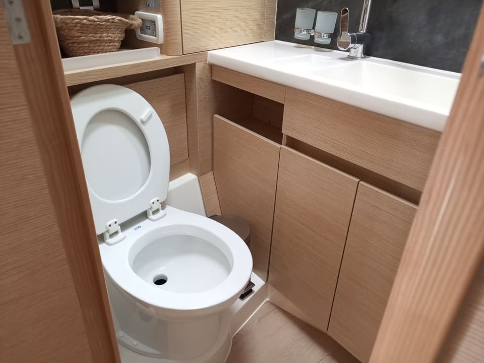 2022 Hanse 508 – deniz tipi tuvalet, açık meşe dolaplar ve beyaz tezgah lavabolu banyo