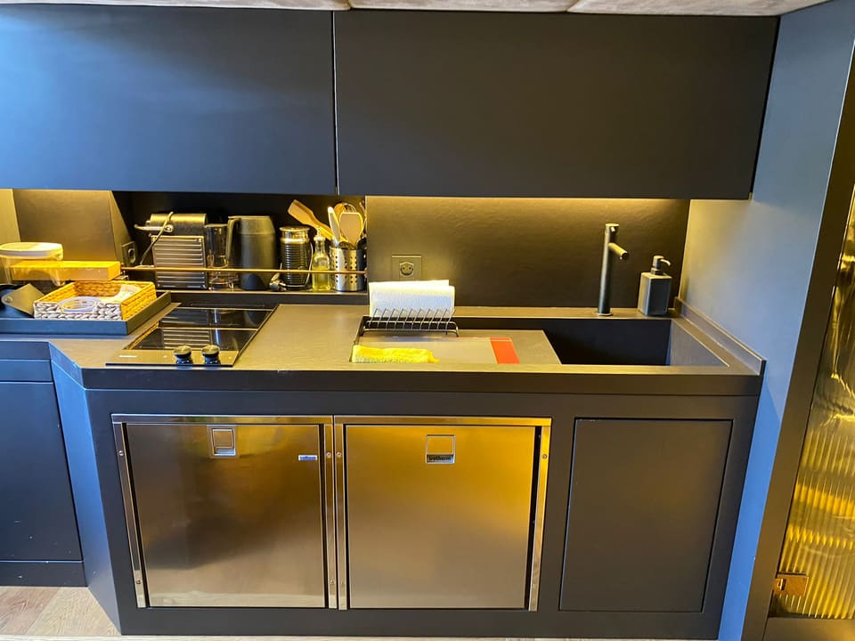 2021 Mazu Yachts 38 – galley with induction hob, sink, stainless steel fridges and warm LED-lit dark cabinetry