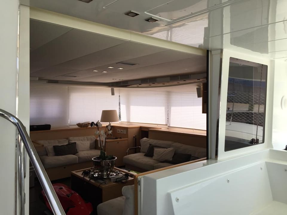 2015 Lagoon 560 S2 – bej koltuklar, minderler, abajur ve jaluzili panoramik pencerelerle salon
