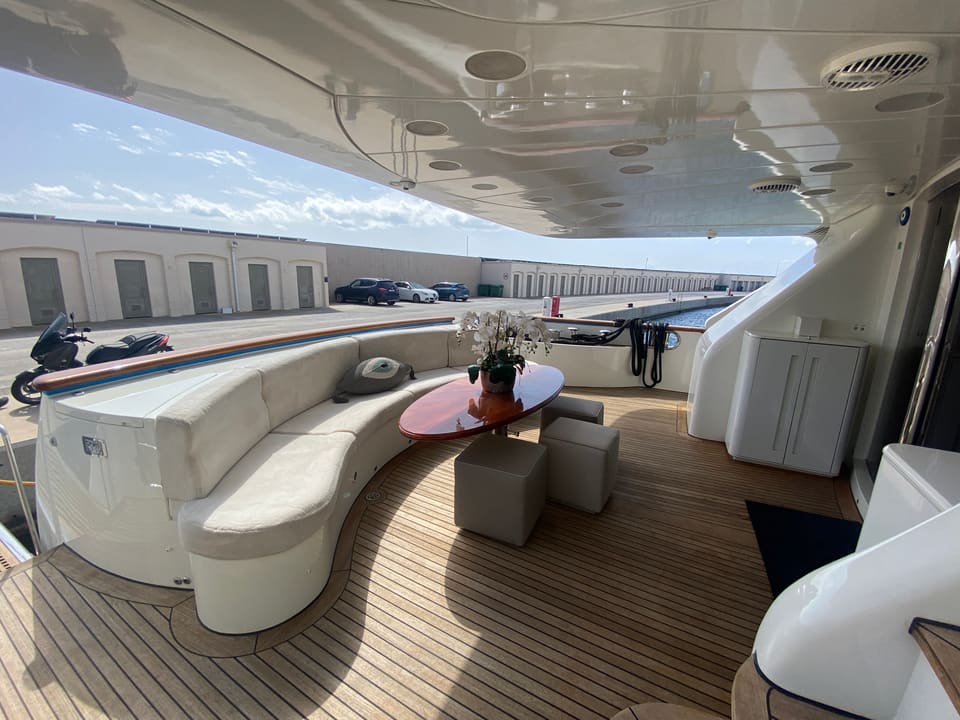 2003 Benetti Classic 115 – covered aft deck with curved settee, teak table, stools and teak decking