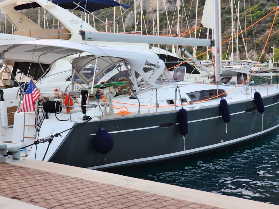 2009 Beneteau Oceanis 54 – koyu gri tekne gövdesi, kokpit üzerinde bimini, usturmaçalar ve kıçta biniş merdiveni