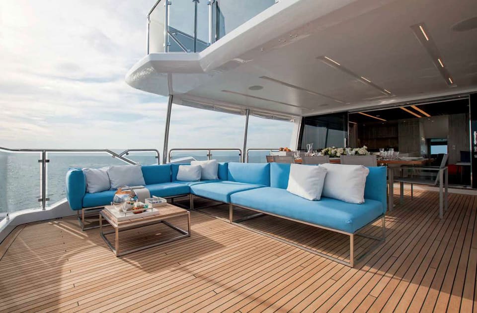 2016 Benetti Tradition Supreme 108 – mavi L koltuk, sehpa ve tik güverteli, salona açılan kıç güverte oturma alanı