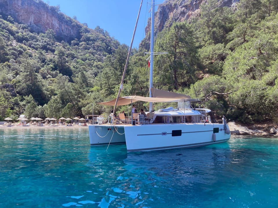2010 Lagoon 400 – catamaran at anchor in turquoise water with shaded cockpit awning and wooded hills behind