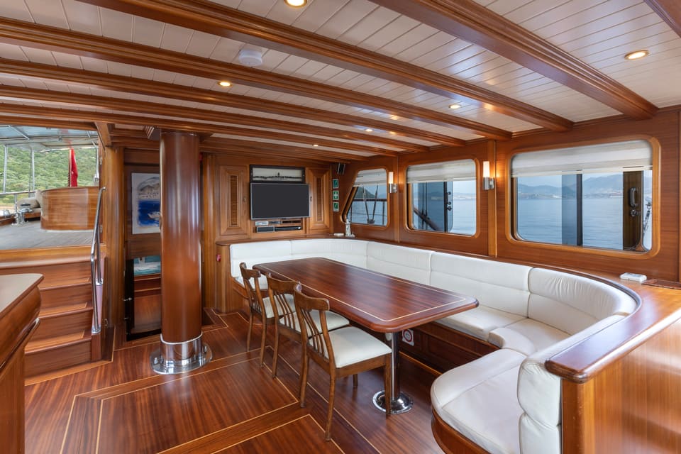 2009 Custom Ketch 31M – wood-panelled saloon with white leather U-shaped sofa, dining table, TV and large windows