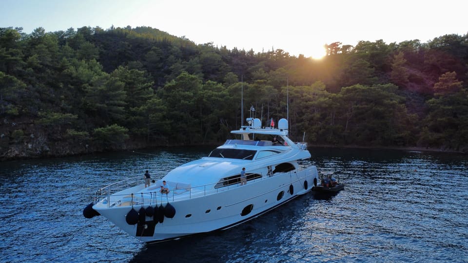 2007 Custom Line 97 – gün batımında ormanlık bir koyda demirli beyaz motoryatın havadan görünümü, yanında servis botu