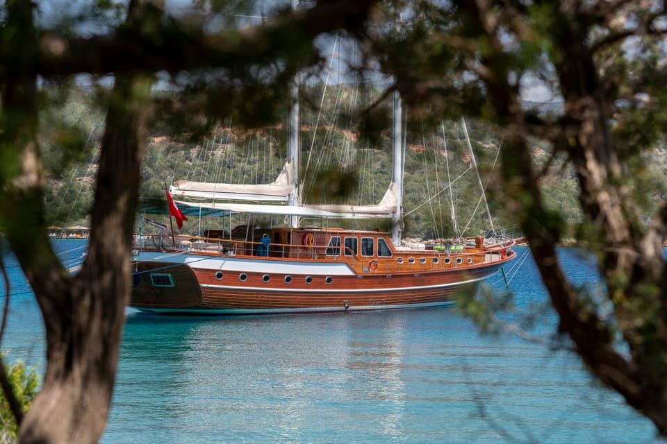 2009 Custom Ketch 31M – wooden gulet-style hull at anchor in turquoise water, framed by pine branches