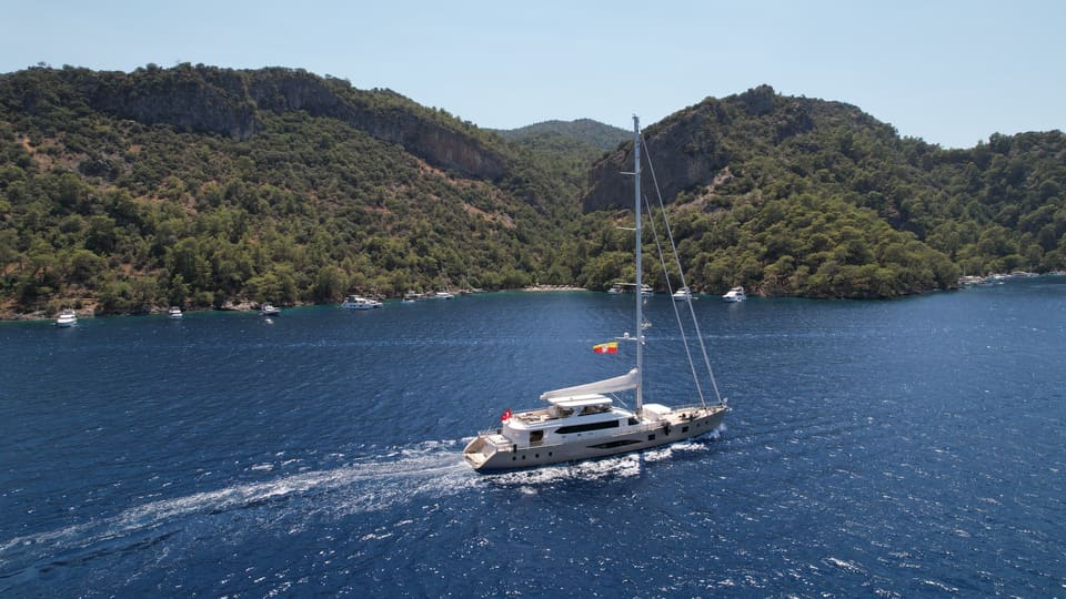 2023 Custom Laminated Motorsailer 41M – aerial view under way with white wake, green wooded hills behind