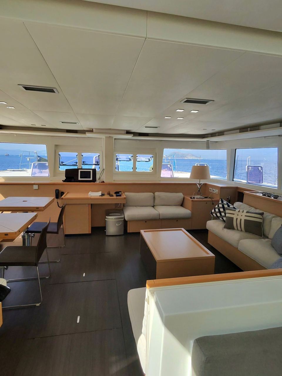 2015 Lagoon 560 S2 – panoramik pencereli aydınlık salon, krem kanepeler, ahşap sehpa ve seyir masası