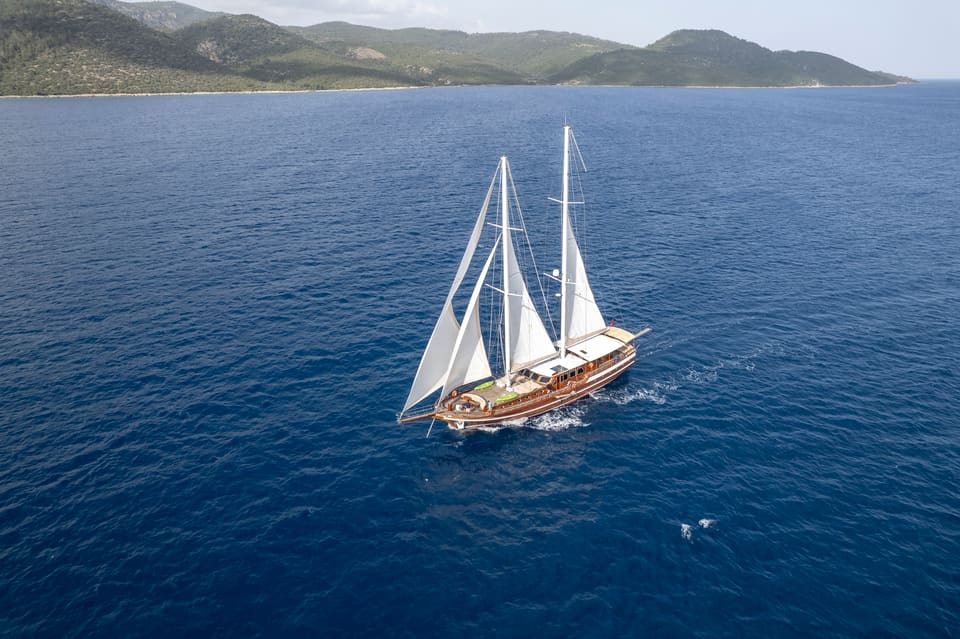 2009 Custom Ketch 31M – aerial view under full sail on open blue sea with wooden hull and teak decks
