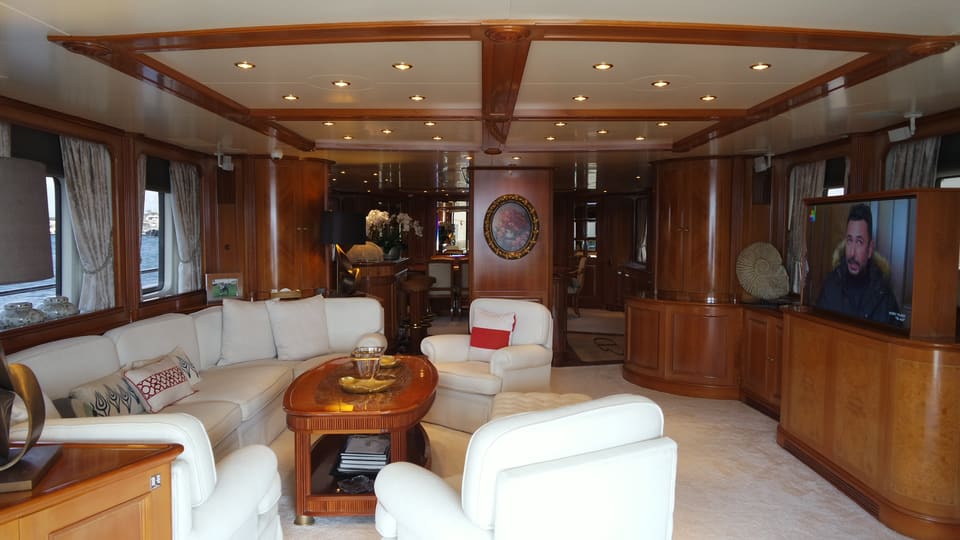 2003 Benetti Classic 115 – main saloon with cream sofas, armchairs, warm wood paneling and TV, dining area beyond
