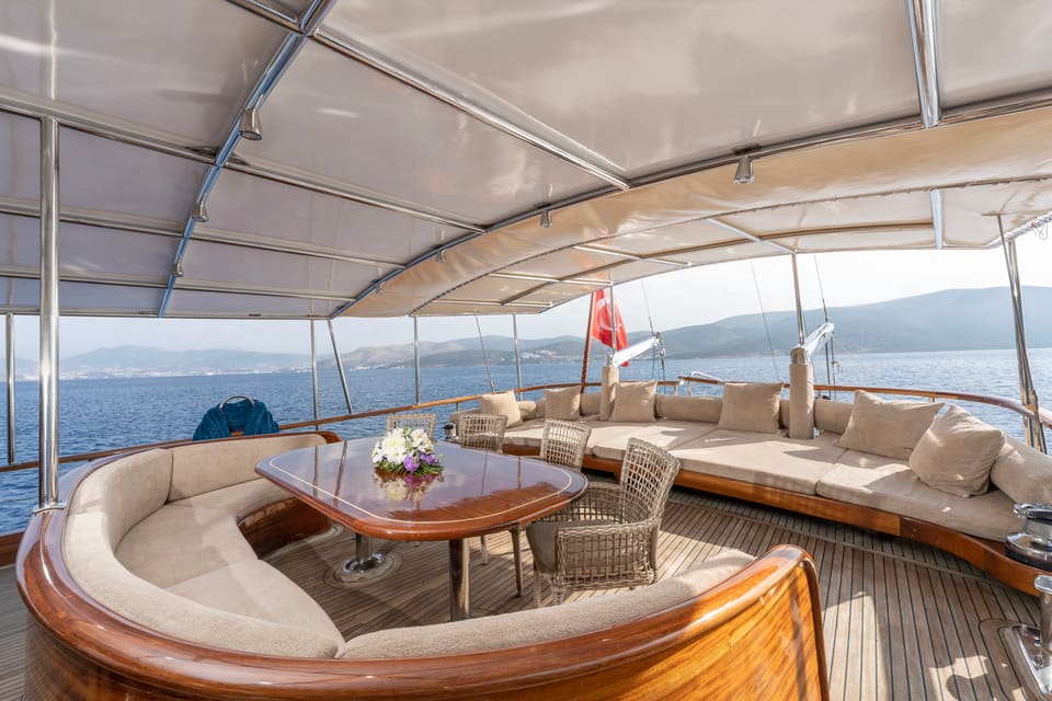 2009 Custom Ketch 31M – shaded aft deck with wraparound sofa, varnished teak table and wicker chairs