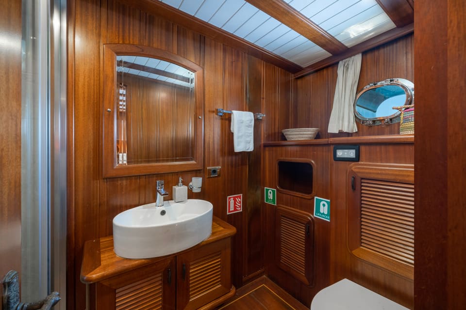 2009 Custom Ketch 31M – wood-panelled bathroom with vessel sink, framed mirror, porthole and louvred cabinets