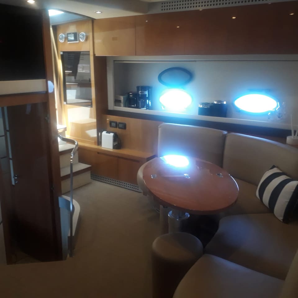 2007 Pershing SpA 62 – krem rengi oval koltuk, yuvarlak ahşap masa, ahşap dolaplar ve alt güverteye inen merdivenli salon