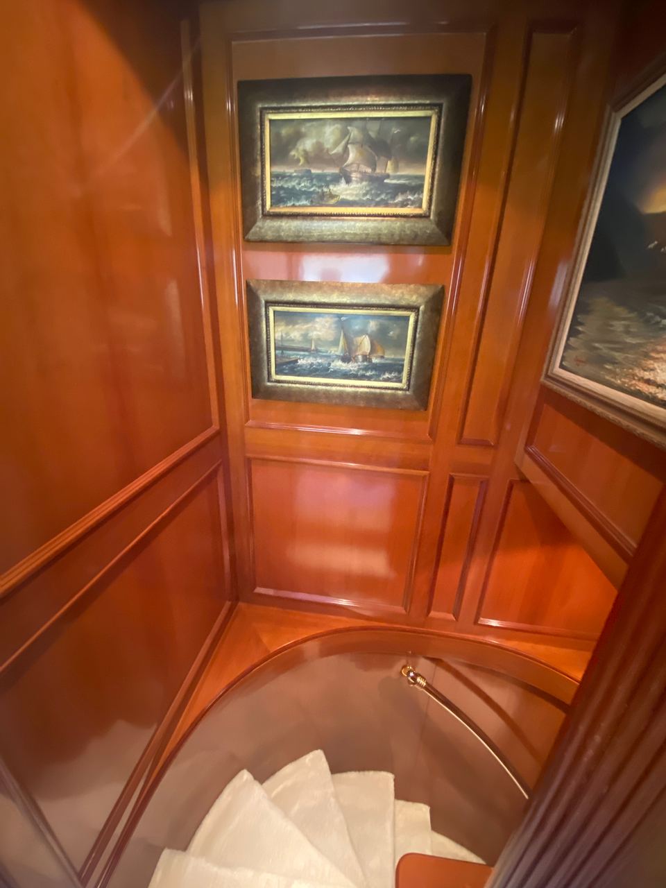 2003 Benetti Classic 115 – spiral staircase with glossy cherry wood panelling and framed marine oil paintings