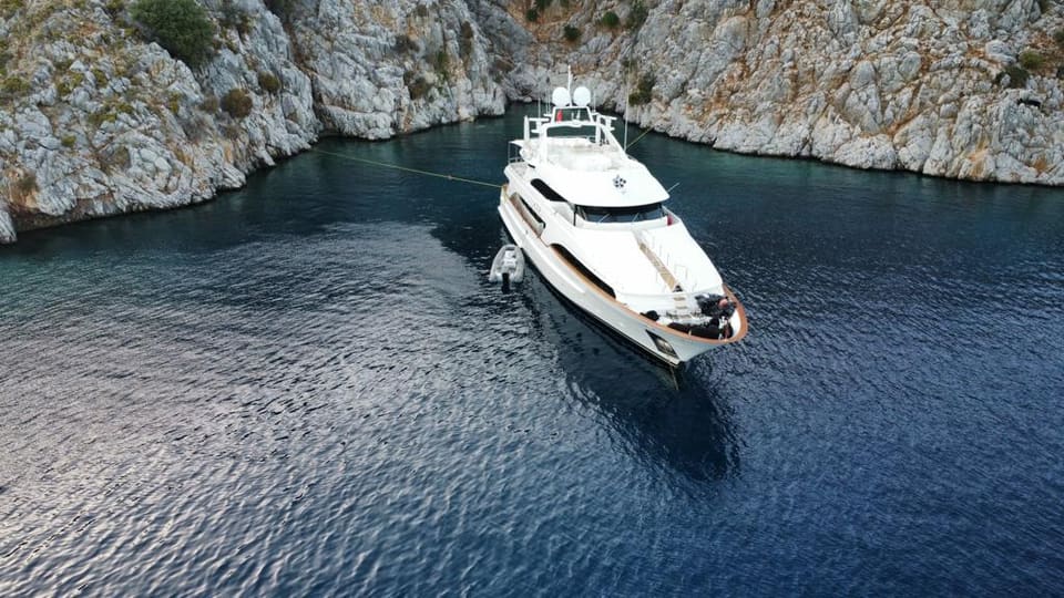 2003 Benetti Classic 115 – aerial view of the motor yacht at anchor in a secluded rocky cove with a stern line ashore