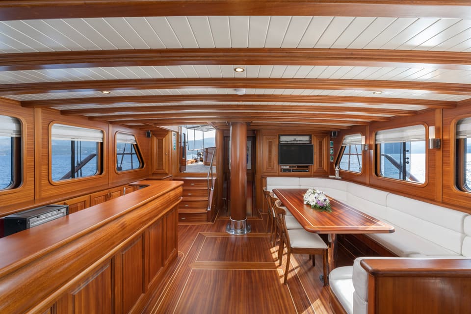 2009 Custom Ketch 31M – teak-panelled saloon with dining table, white L-shaped sofa, bar counter and panoramic windows